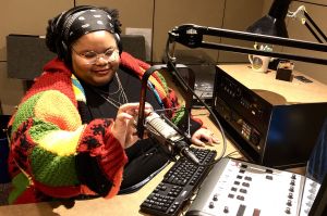 Daniella Richardson with headphones on, sitting at desk with mic and mixing board