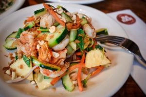 A salad comprised of sliced cucumbers, carrots, and shrimp on a white plate