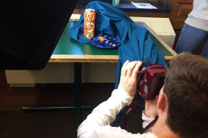 Student photographing and arrangement of a tea can and candy with a teal cloth on a table.  A lighting device is in view.