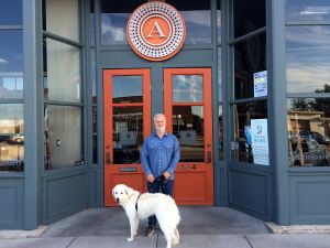 Shawn Askinosie standing in front of a storefront with a large white dog.