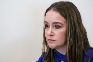 Cora Steinmetz at a press conference pictured in front of a white backdrop. Steinmetz is a White woman with long, dark brown hair.