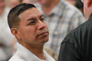 Diego Morales listens to someone speak. Morales is a Hispanic man with black hair. He is wearing a white polo shirt.