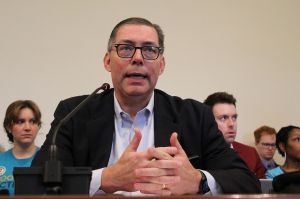 Jonathan Ingram speaks in front of the Senate Appropriations Committee. He is a White man with dark hair, wearing a suit with a purple shirt.