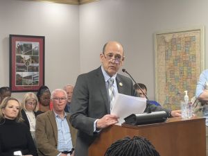 A man speaking at a podium with about a dozen people behind him