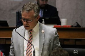 J.D. Prescott is a White man with brown hair. He is wearing a suit and tie.