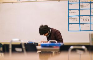 man in brown sweater sitting and writing in classroom