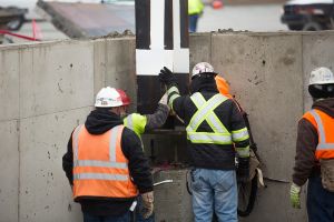 Construction workers at the Kokomo plant guide the first beam into place after a ceremonial signing. They wear reflective gear and hard hats.