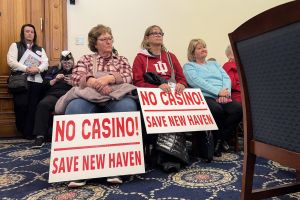 Two women sit in a committee room, each with a sign in front of them that reads "No Casino! Save New Haven"