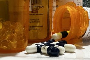 Several prescription pill bottles sit on a white counter top. One rests on its side with white and black capsules spilling out of it. 
