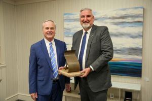 Eric Holcomb is a White man with white hair and beard. He is wearing a tan suit and blue tie.