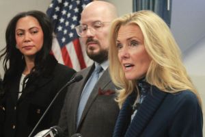 Mike Bohacek stands behind a podium with one hand outstretched. He wears a black and yellow tie with a white button down shirt.