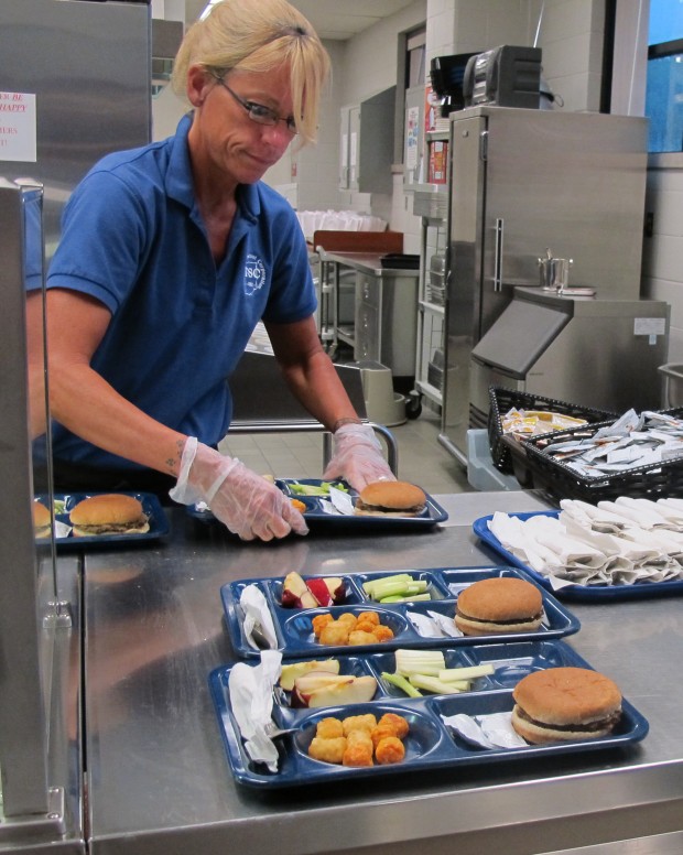 In this 2012 photo, a cafeteria worker prepares lunch trays for first grade students. (Elle Moxley/StateImpact Indiana)